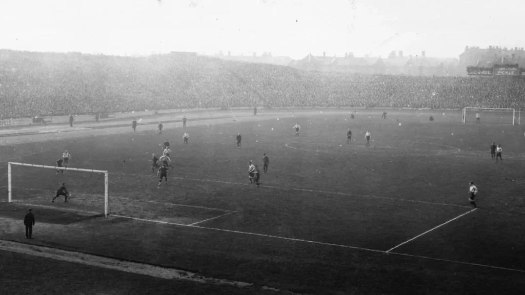 A grainy black and white image of a football ground with players on the pitch.
