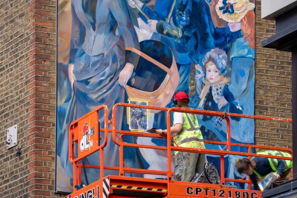 een kunstenaar op een hoogwerker, boven de straat, die een Renoir-muurschildering aanbrengt op een muur in Carnaby Street