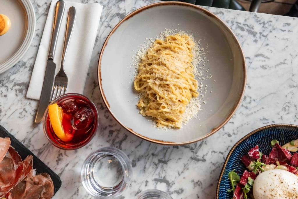 Eine Luftaufnahme eines Esstisches mit Tellern voller Pasta, Wurstwaren und einem Negroni