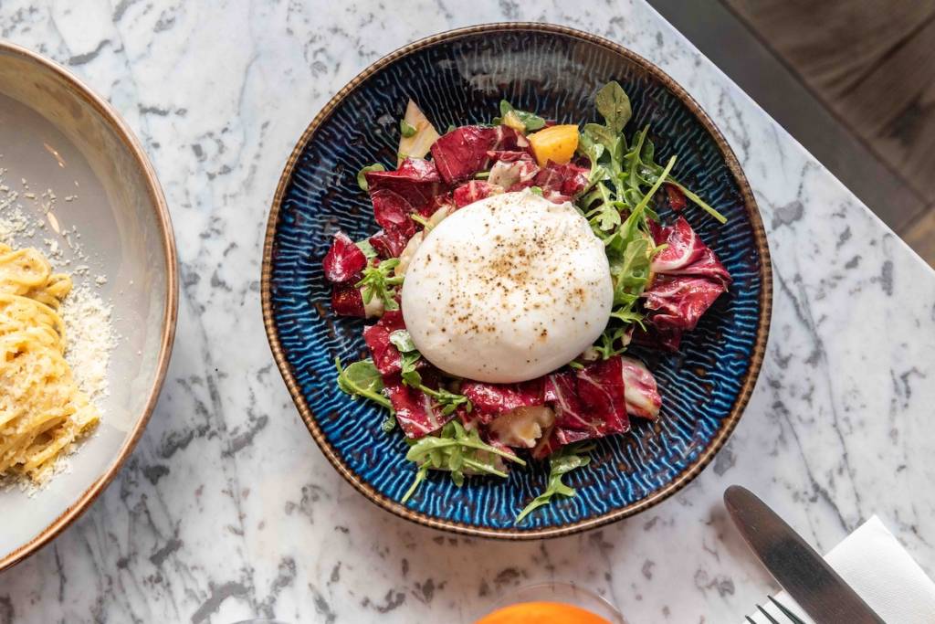 Ein Teller Burrata auf buntem Salat, serviert auf einem Marmortisch