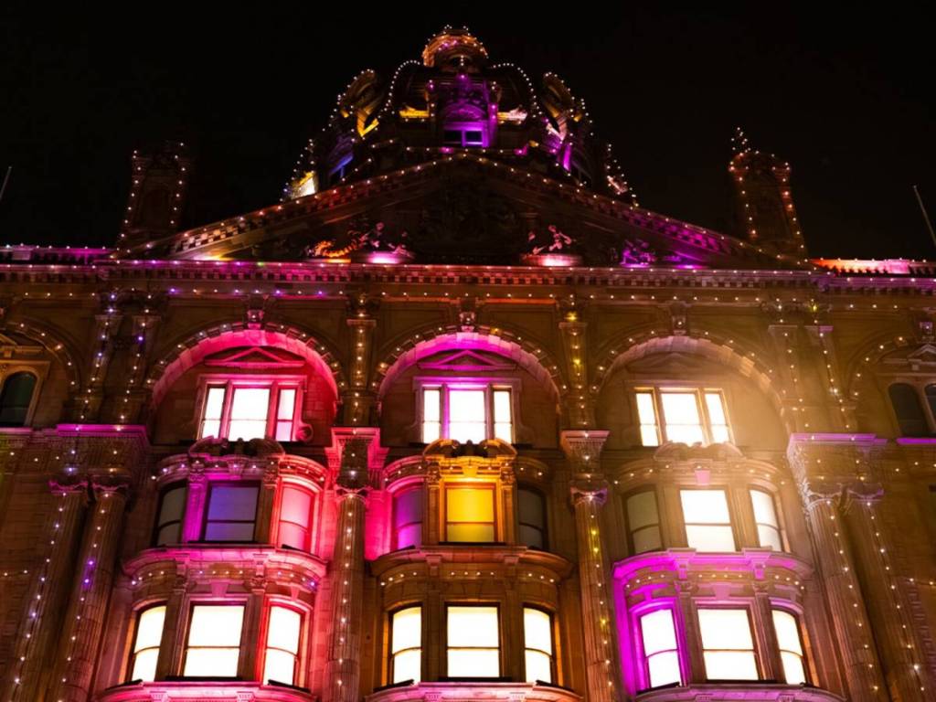 die Fassade des Kaufhauses Harrods, die nachts mit einer farbenfrohen Diwali-Lichterkette beleuchtet ist
