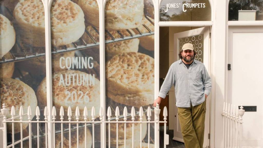 un uomo era in piedi fuori da un crumpet café di Jones’ Crumpets, con le vetrine ricoperte da grandi adesivi a forma di crumpet