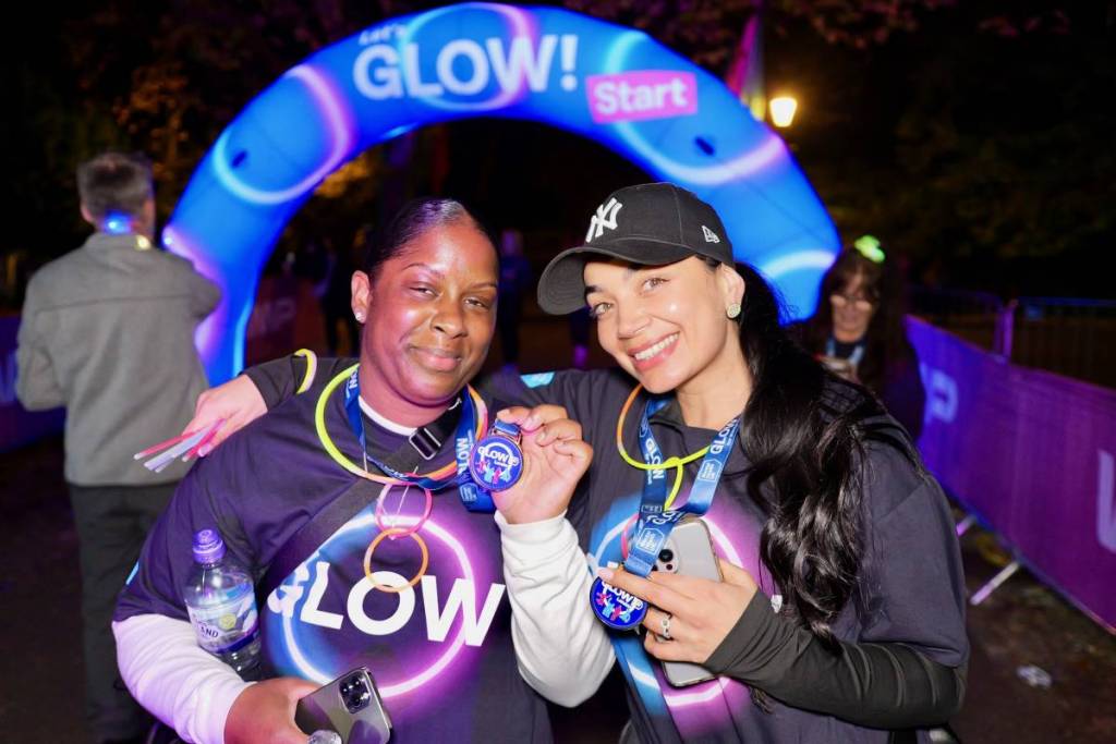 due persone che posano di notte con le loro medaglie, con dei bastoncini luminosi al collo, dopo aver completato una passeggiata notturna di beneficenza