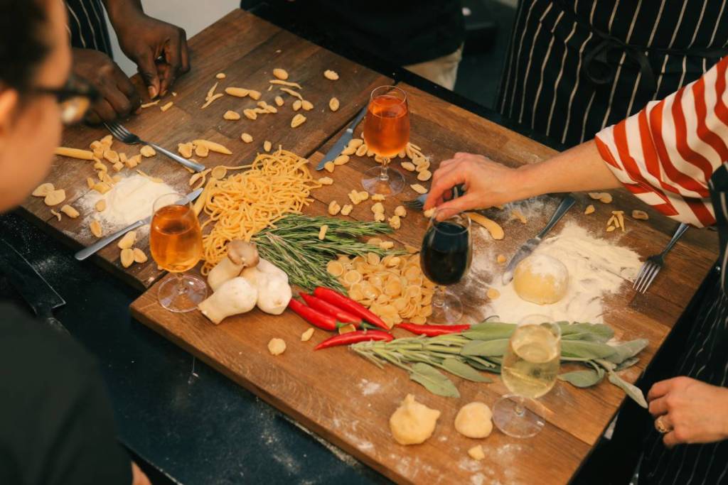 persone che preparano la pasta durante un laboratorio, su un tavolo ricoperto di pasta, bicchieri di vino e ingredienti per la pasta