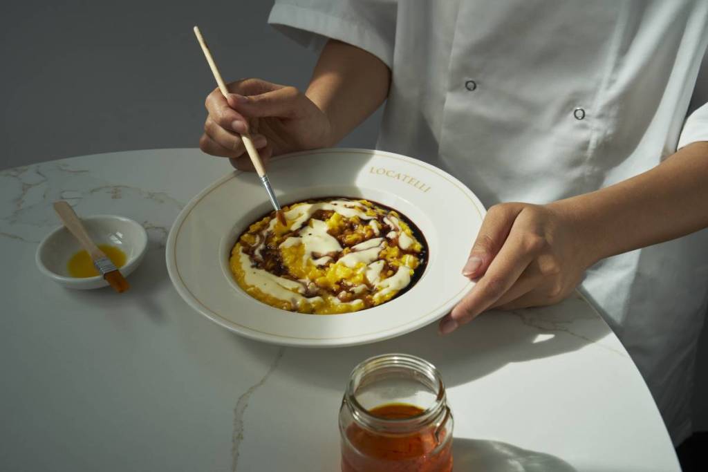 uno chef che dà gli ultimi ritocchi a un piatto di risotto ispirato a Renoir, usando un pennello