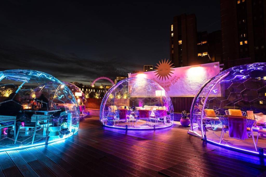 A rooftop bar with protective bubbles covering the tables and colourful lighting