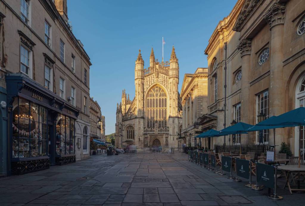 The exterior of Bath Abbey plus rows of coffee shops on the street in front
