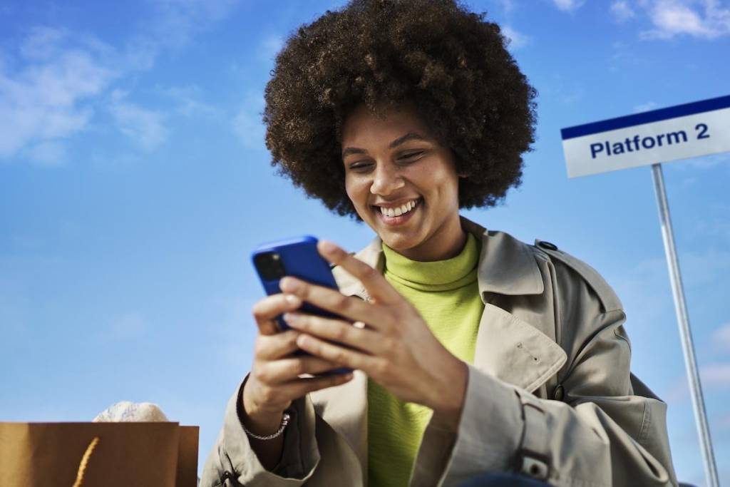 A woman smiling at her phone with a platform sign in the background