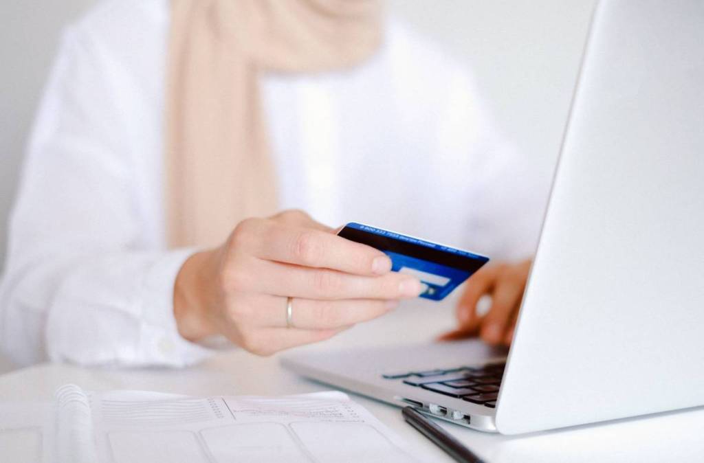 Nahaufnahme einer Person, die eine Kreditkarte in der Hand hält, während sie mit einem Laptop online einkauft.