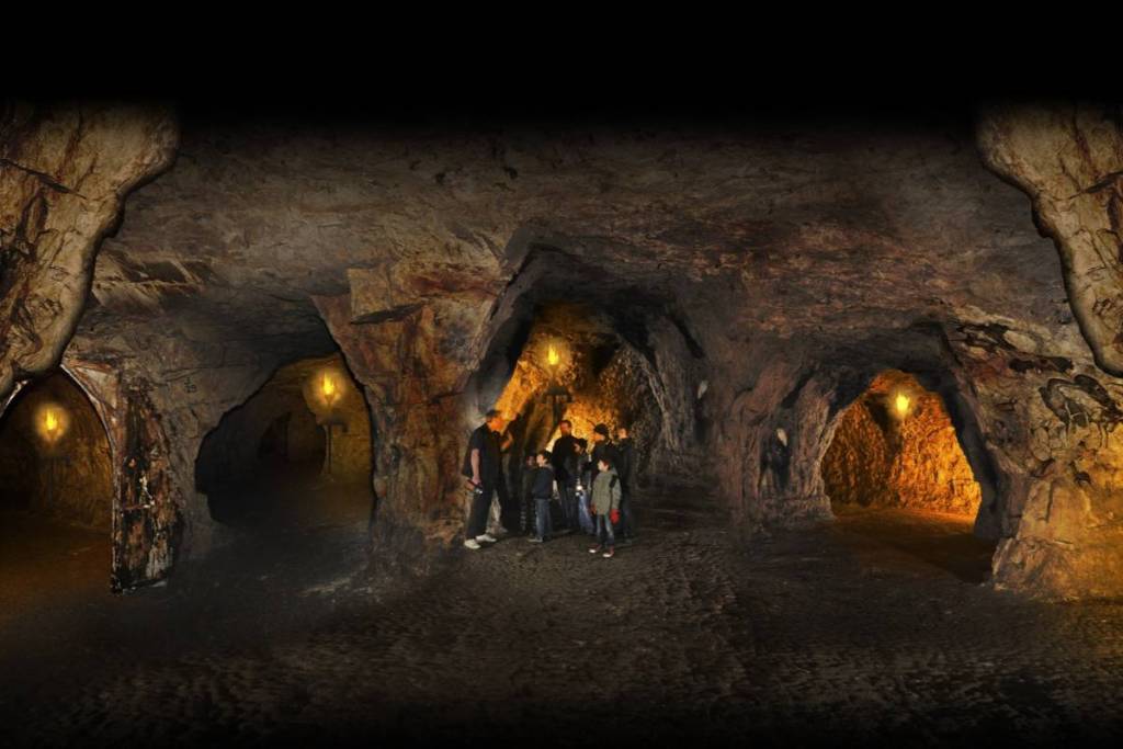 a group of people standing in the middle of a room inside a vast network of caves, illuminated by lanterns