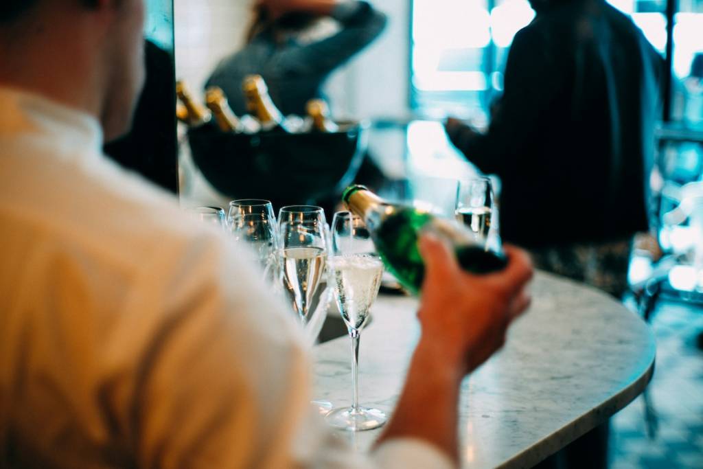 A person is pouring champagne into a glass, with several full glasses next to it on a table