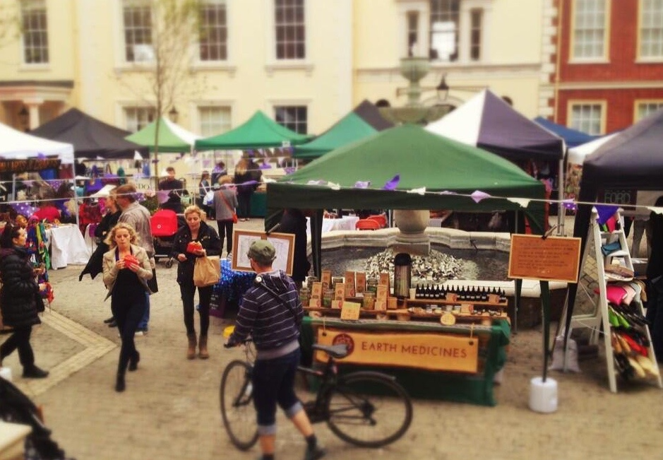 A busy weekend market, with several people walking through the stalls and a man pushing a bike