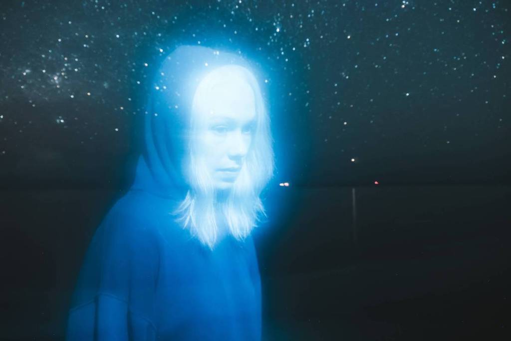 Pressefoto von Phoebe Bridgers vor dem Hintergrund von Sternen und Himmel, auf dem die Künstlerin blau leuchtet