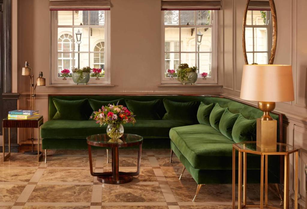 Die Lobby eines Londoner Luxushotels mit einem grünen Sofa und einem Couchtisch, auf dem eine Vase mit Blumen steht