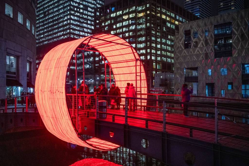 Un puente rodeado de un espectáculo de luces rojas circulares. Al fondo se ven edificios con muchas ventanas. 