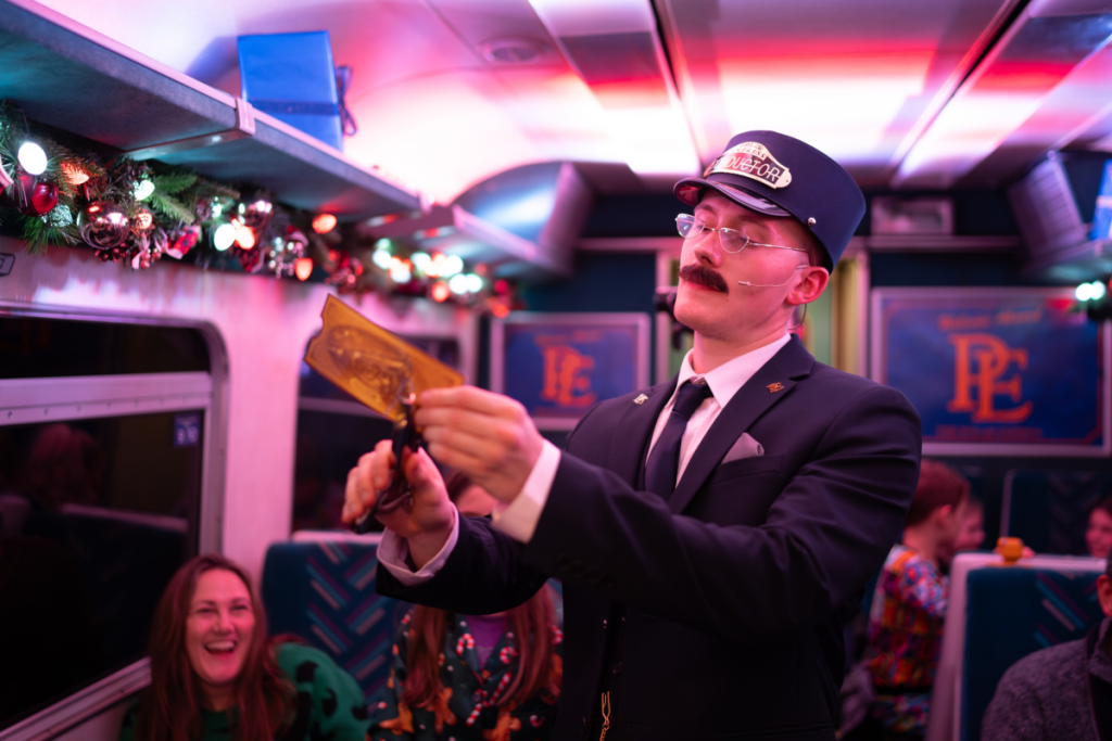 A train conductor punching a golden ticket on board the Polar Express Experience