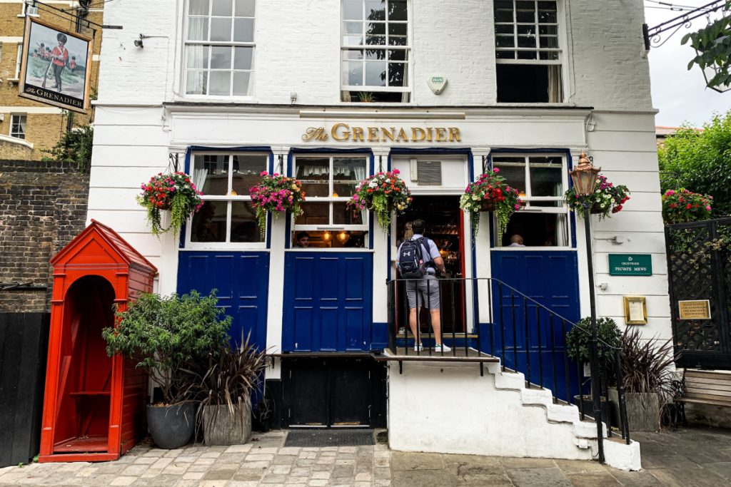 alguém a entrar num pub em Londres com uma fachada azul e branca e cestos de flores pendurados na frente