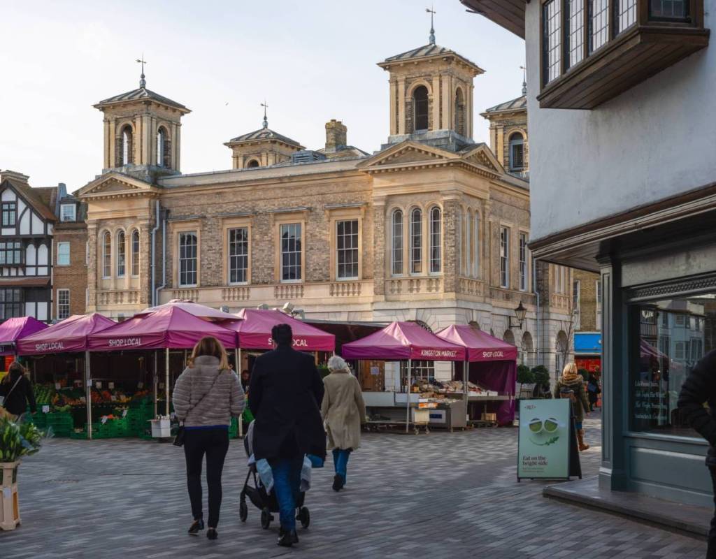 Kingston upon Thames, London, Großbritannien, 25. Januar 2024. Menschen spazieren bei Tageslicht über den Marktplatz von Kingston upon Thames, auf dem lila Zelte, Stände mit regionalen Produkten und das historische Rathausgebäude zu sehen sind.