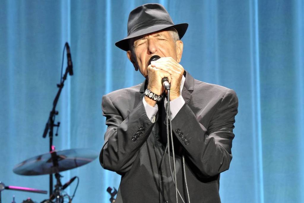 Leonard Cohen zingt op het podium in pak en hoed