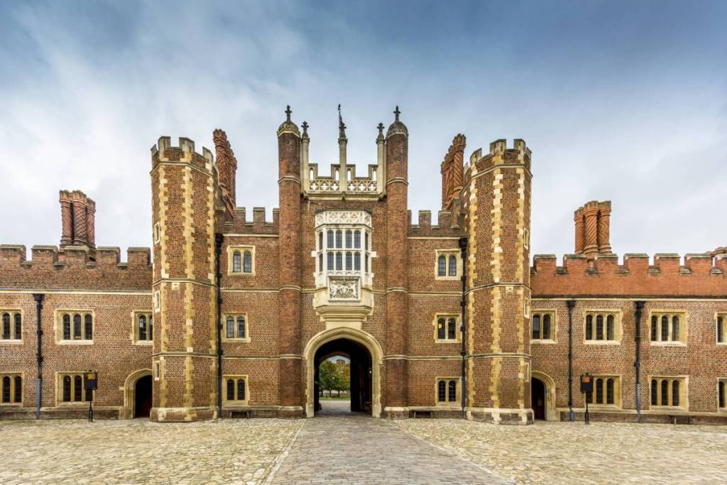 Palacio de Hampton Court, un antiguo edificio de ladrillo con torretas, muchas ventanitas y un arco en el centro.