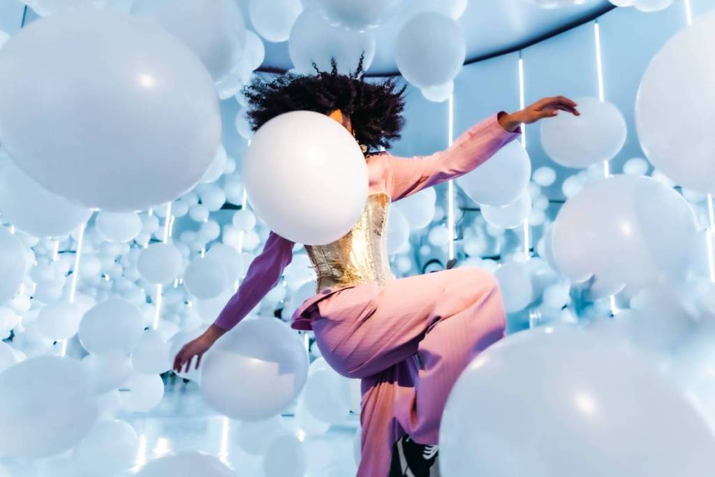 Una persona che salta tra palloncini bianchi all’installazione artistica “Invisible Ballet” nell’ambito dell’esperienza “Euphoria” del Balloon Museum
