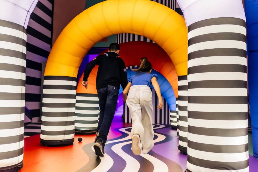Due persone viste di spalle mentre corrono in un colorato labirinto gonfiabile, una delle installazioni artistiche dell’esperienza Euphoяia al Balloon Museum