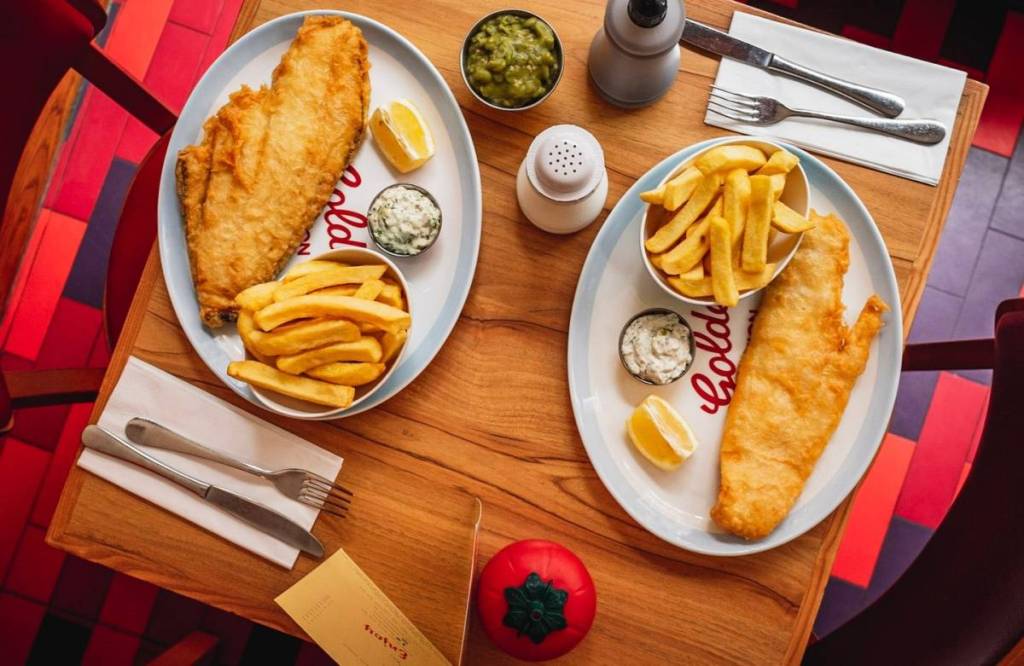 una vista dall’alto di due piatti di fish and chips con alcuni condimenti su un tavolo