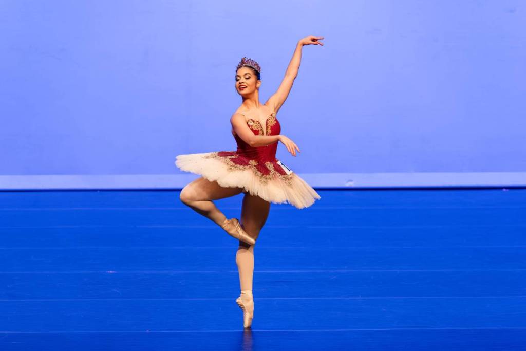 A ballerina in a red and white tutu, mid-dance against a blue background