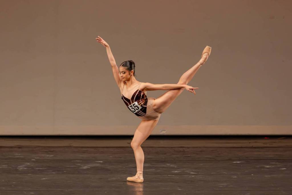 A ballerina mid-dance against a beige background