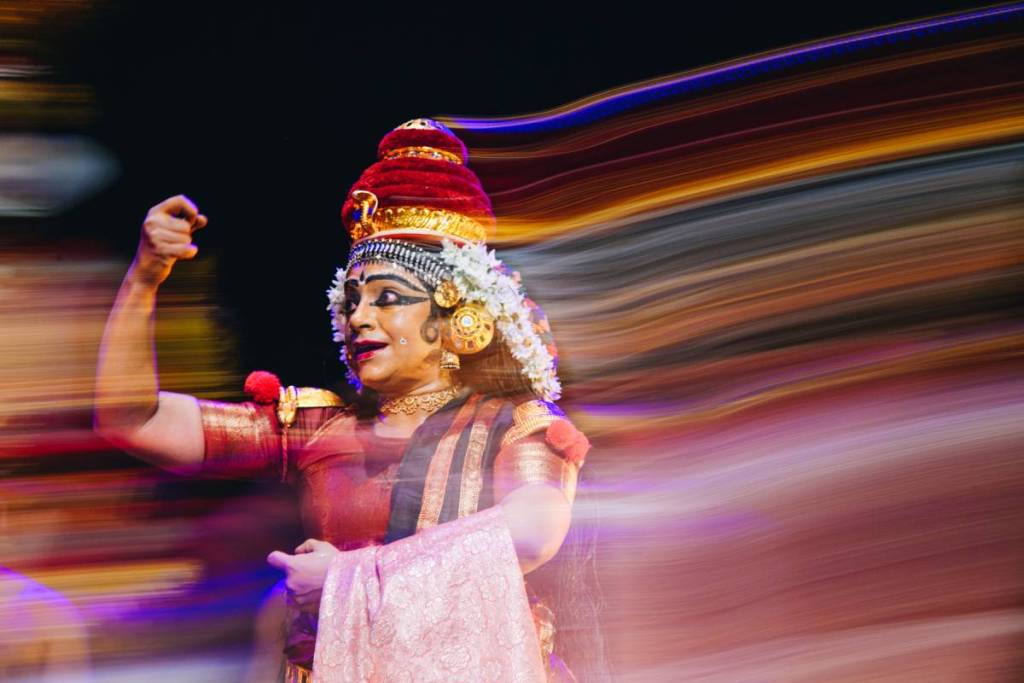 a blurry image of a performer onstage in a strong pose flexing an arm