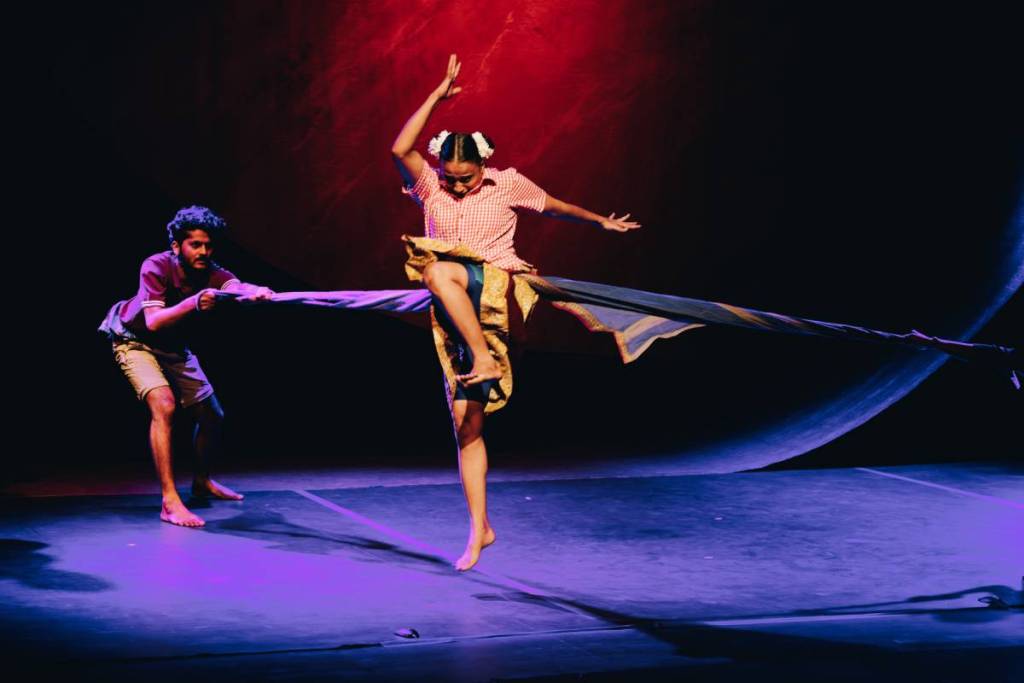 a performer with a rope wrapped around them trying to break free of bonds held by other perfomers onstage