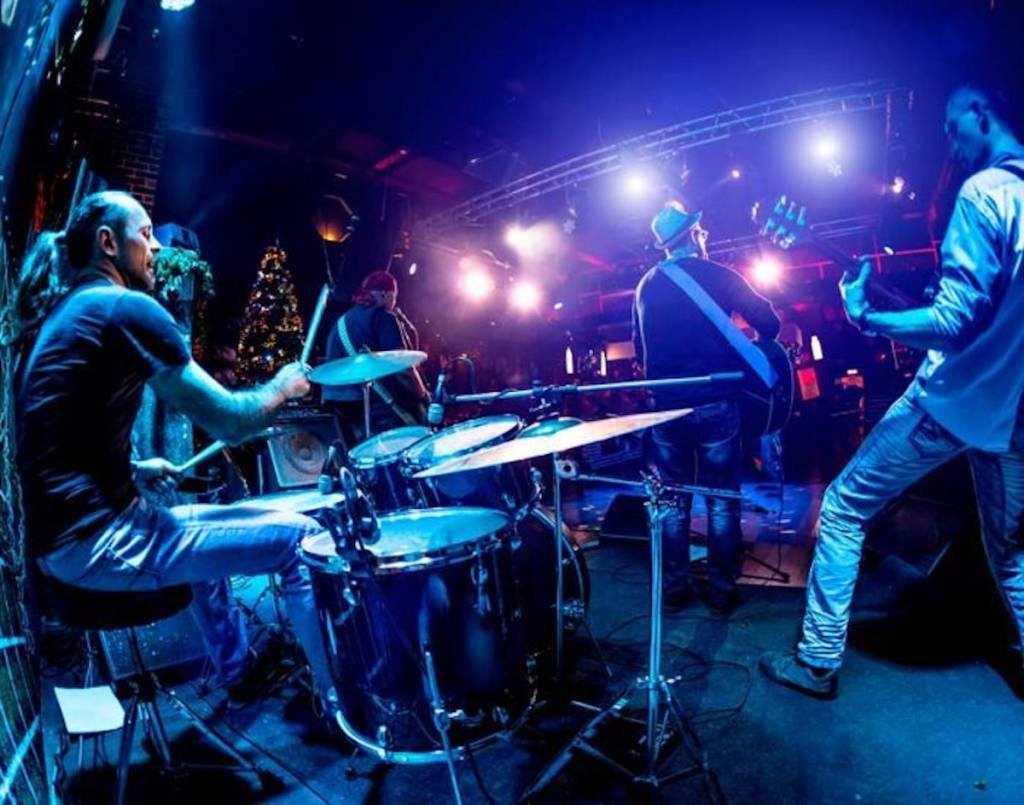 Musicians playing instruments on a small stage, playing the drum and guitars