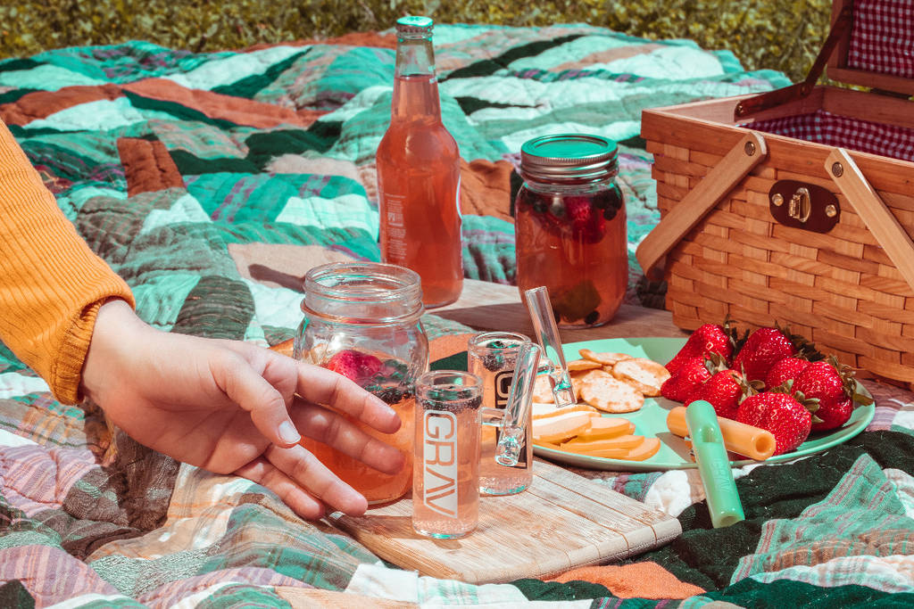A picnic blanket on grass with a picnic box, drinks and glasses