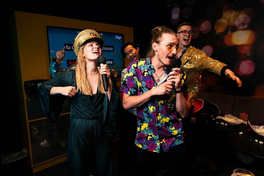 Several people sing karaoke at a karaoke bar.