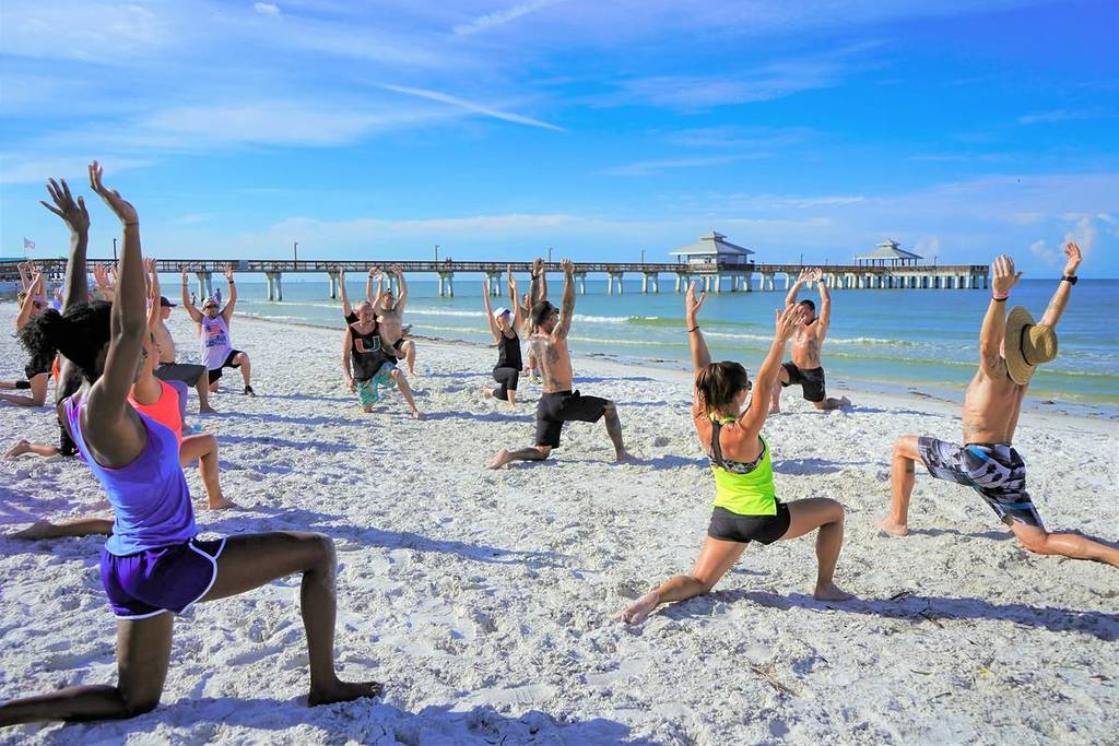 People do yoga on a beach.