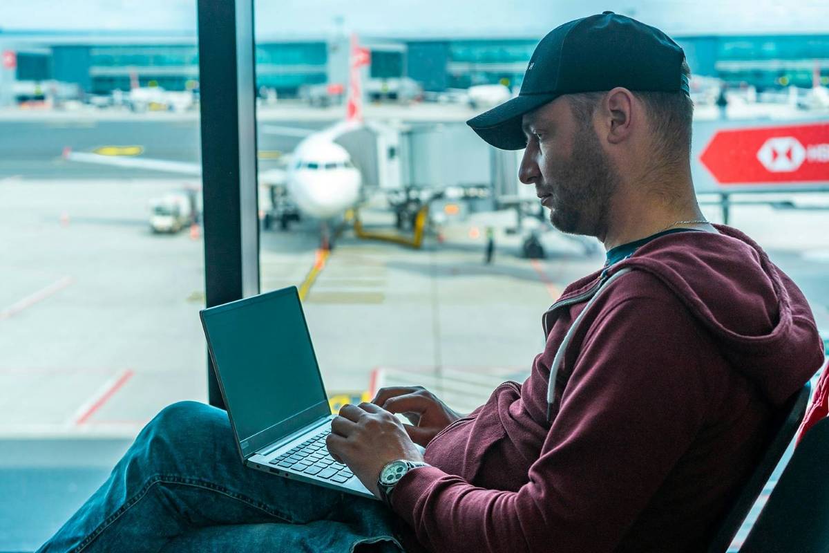 Man working on laptop at the airport with airplane in the background.