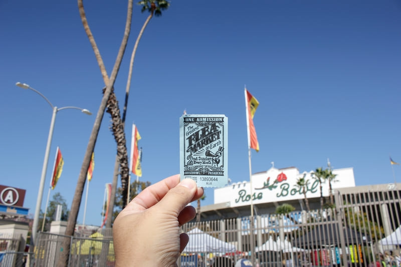 A hand holds up a ticket in front of Rose Bowl Flea