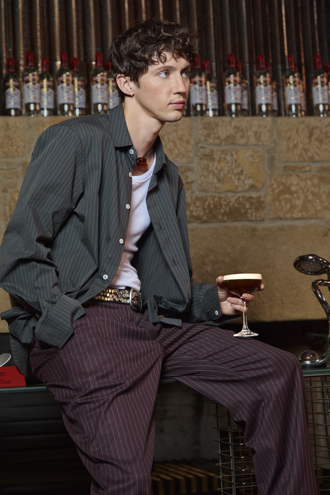 Troye Sivan sits surrounded by Smirnoff bottles with a martini in hand