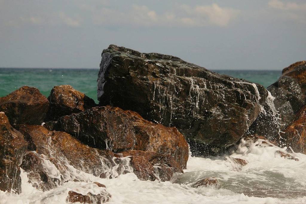 Waves crash across rocks in the sea.