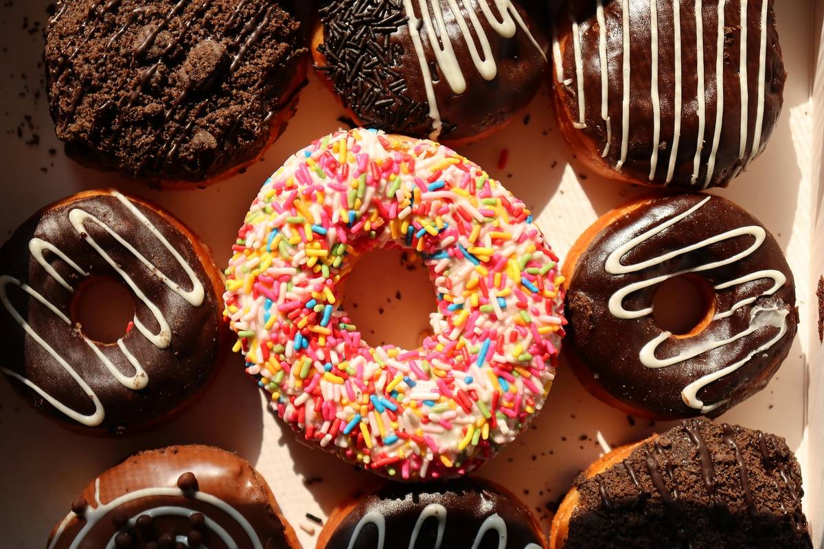 A box filled with iced doughnuts, with a pink one in the middle of 8 chocolate ones.