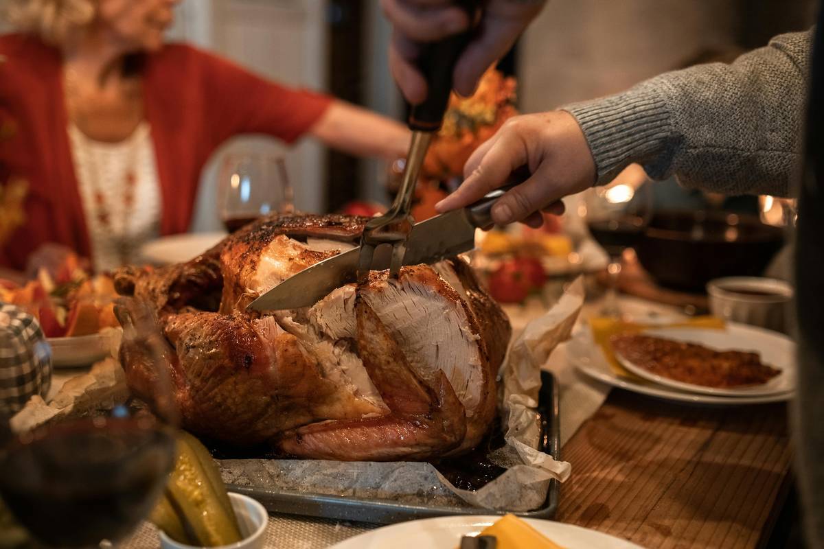 A turkey sits on a table and someone's is seen cutting into it.