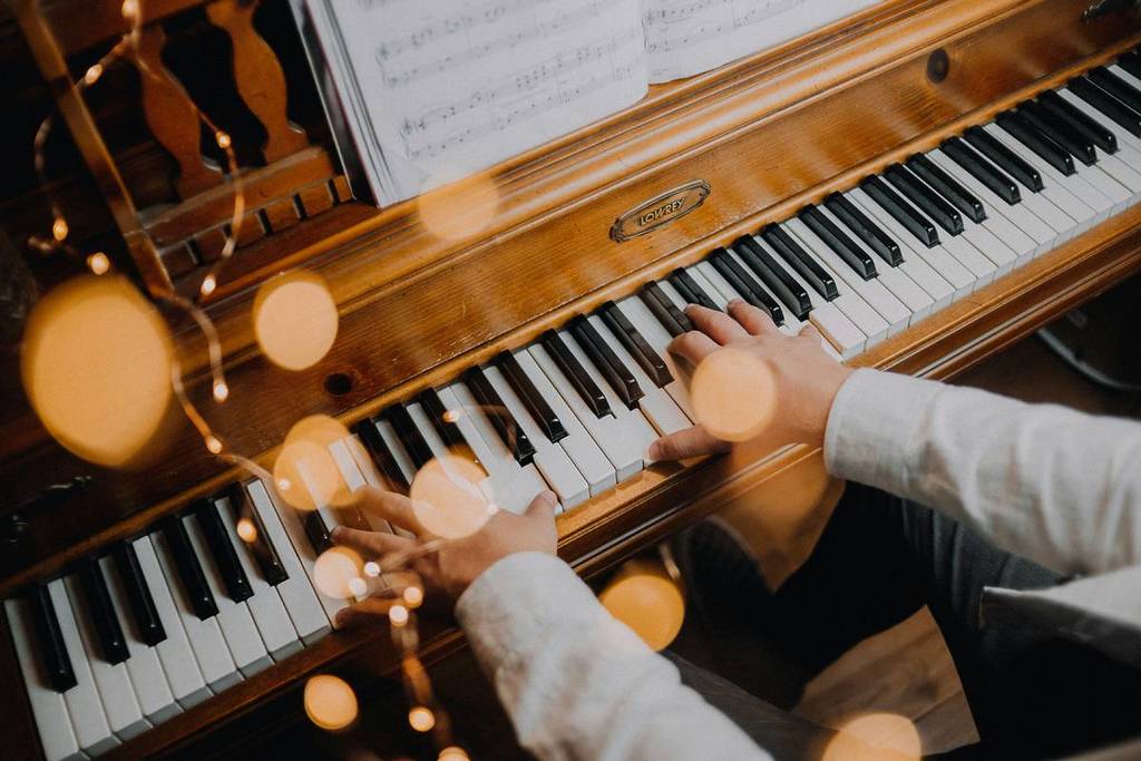 A person plays a piano with fairy lights around.
