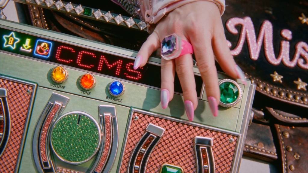 a woman's hand with long pink nails adjusts the dial on a colourful retro stereo with jewels and horseshoes on it