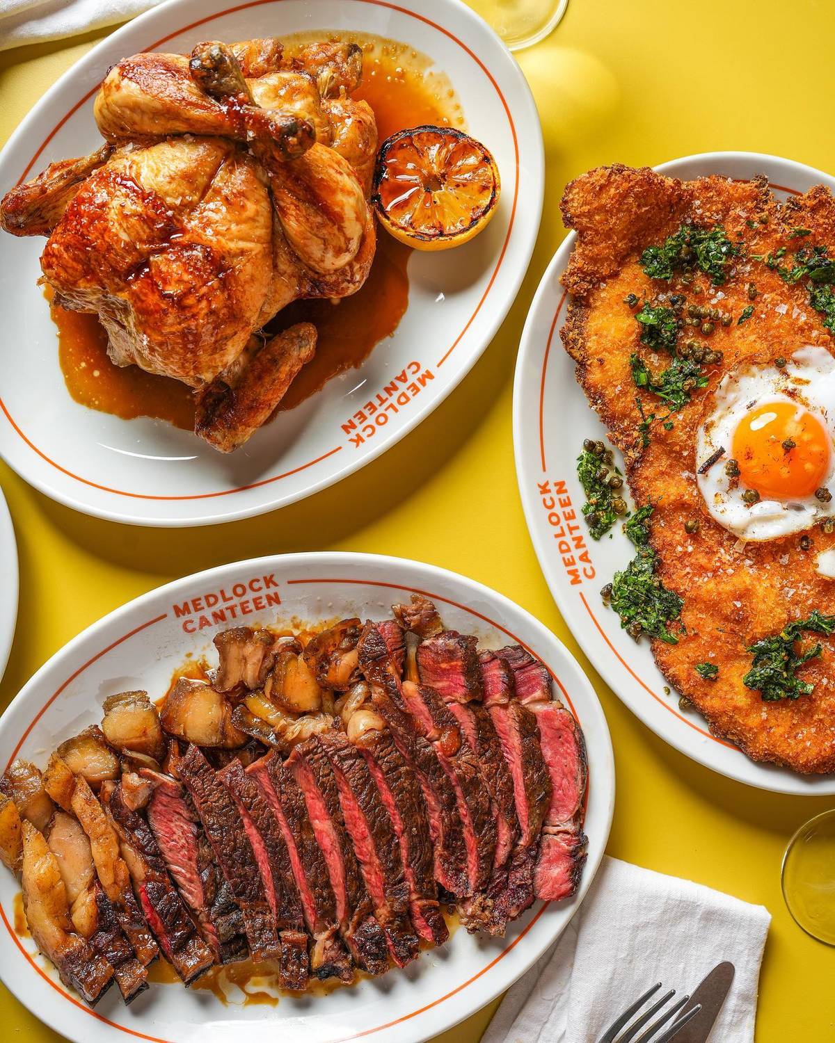 whole-rotisserie-chicken-plate-of-sliced-rare-steak-next-to-plate-with-large-schnitzel-with-fried-egg-on-top
