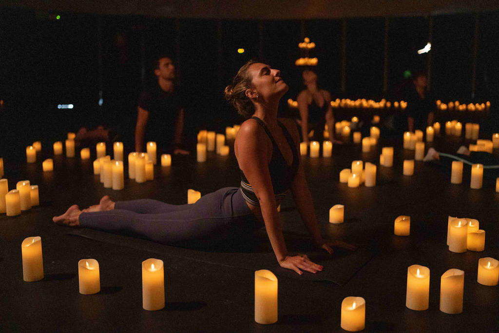 A person practises yoga, surrounded by candles at Mindful Glow.
