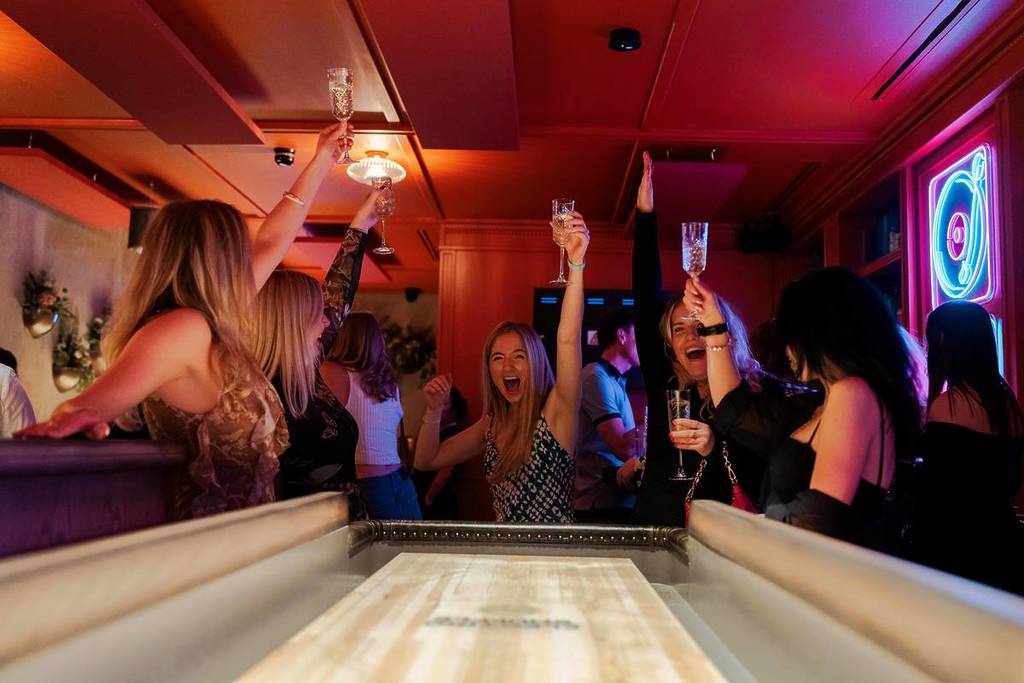 girls celebrating with champagne glasses playing shuffleboard at electric shuffle