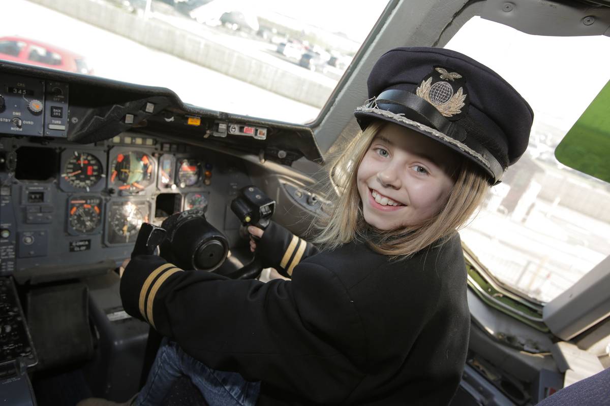 young girl wearing pilot hat in cockpit at Runway Visitor Park
