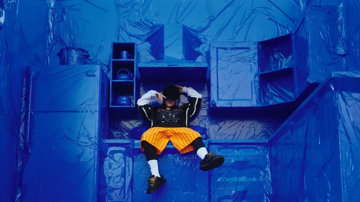billie-eilish-sat-down-on-blue-background-with-bright-yellow-shorts-tour-coming-to-manchester-co-op-live