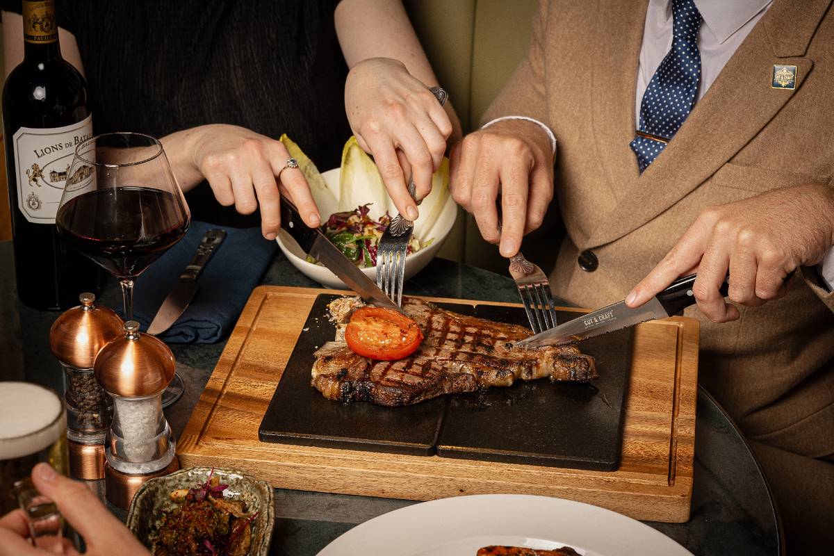 couple cutting into steak on board at the cut and craft