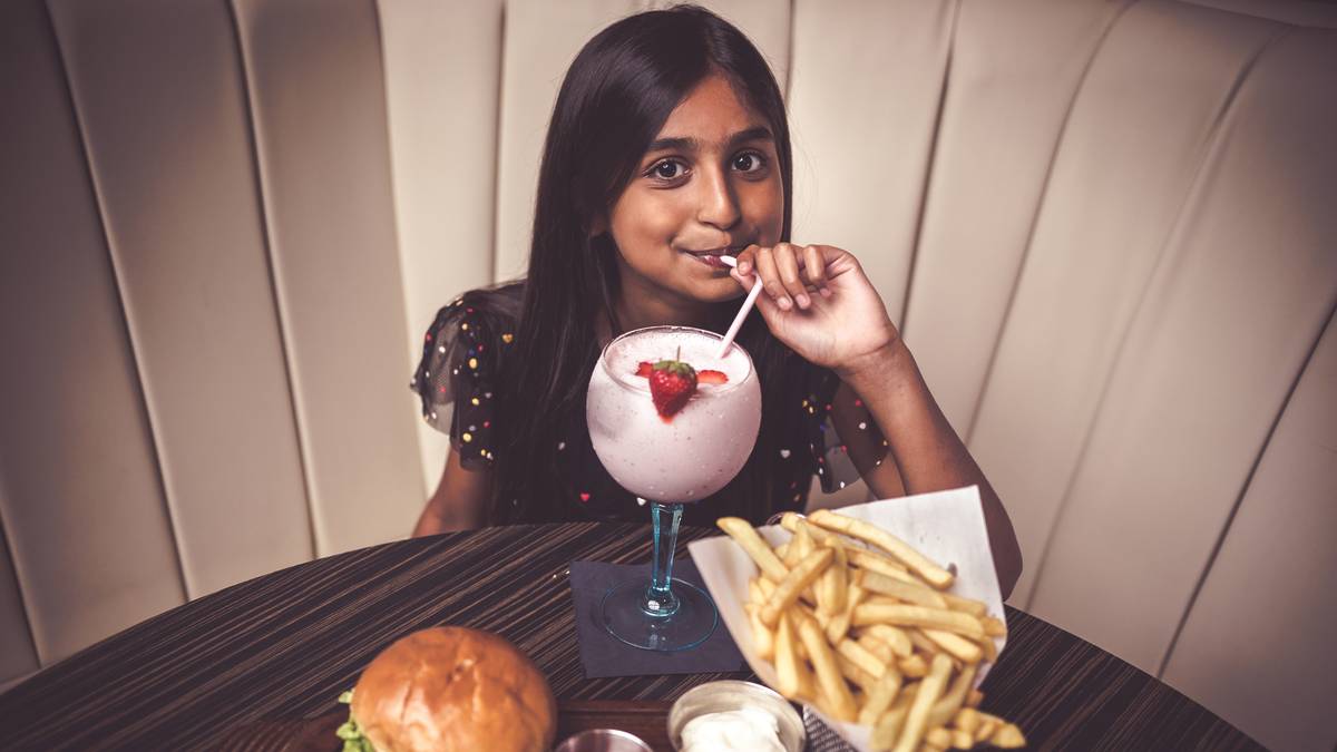 girl drinking strawberry milkshake next to burger and fries at zouk manchester, where kids eat free this summer